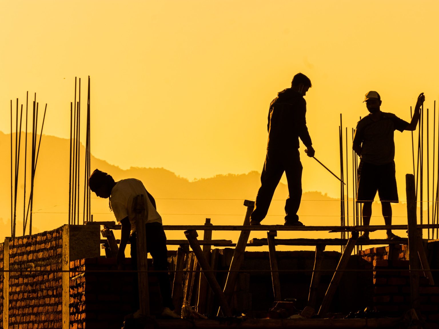 Silhouetted workers on a construction site at sunset, highlighting the manual labor involved.